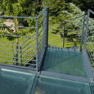 Balcon moderne avec sol en verre trempé et garde-corps métallique offrant une vue imprenable sur le jardin verdoyant