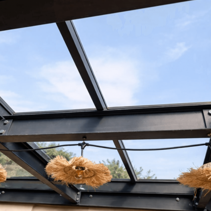 Pergola moderne avec toit en verre trempé transparent et lampes suspendues créant une ambiance chaleureuse en plein air