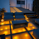 Terrasse moderne en verre éclairée de manière chaleureuse, avec des coussins confortables et une table basse, créant une ambiance accueillante pour un espace extérieur intime et lumineux.