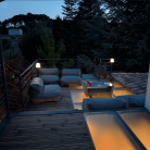 Terrasse avec sol en verre trempé et éclairage doux créant une ambiance accueillante, décorée avec des canapés confortables et vue sur la nature environnante