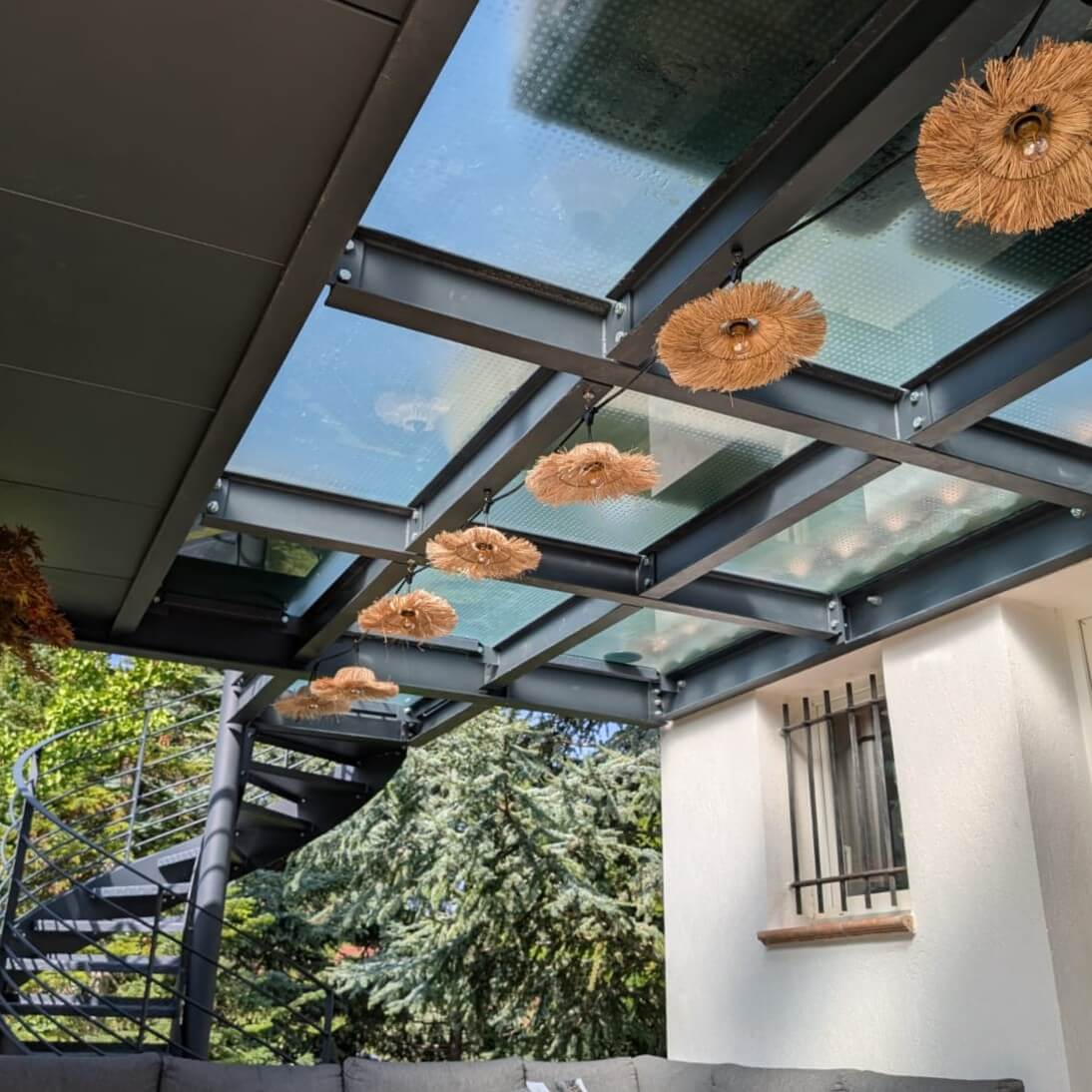 Pergola en verre pour terrasse avec toit transparent et éclairage décoratif en fleurs séchées, offrant une atmosphère élégante et fonctionnelle à l'espace extérieur.